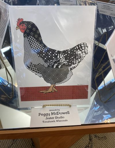 A framed picture of a chicken displayed in a glass case, showcasing its vibrant colors and intricate details.