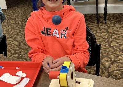 A young girl sits at a table, engaged with a toy machine designed for STEAM learning activities.