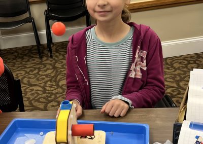 A young girl sits at a table, engaged with a toy machine designed for STEAM learning activities.