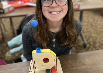 A cheerful young girl sits at a table, beaming as she engages with her completed STEAM build.