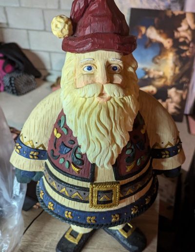 A charming folk Santa Claus figurine with a fluffy white beard and a classic red hat, perfect for festive decor.