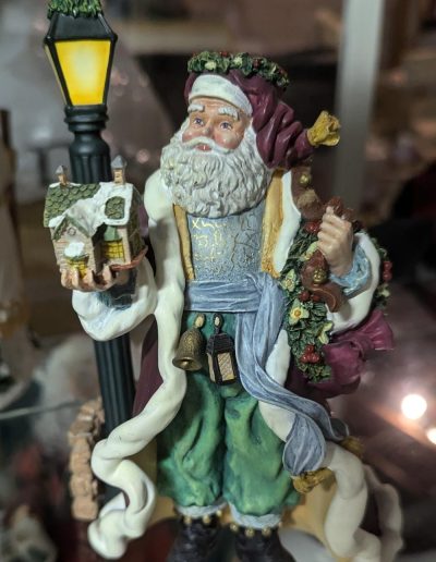 A figurine of Santa Claus holding a lamp beside a charming house, evoking a festive holiday spirit.