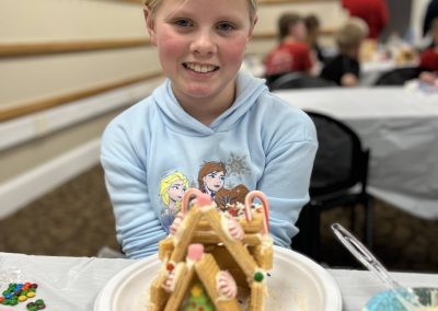 A smiling young girl showcases her delightful gingerbread house, a testament to her creative baking skills.