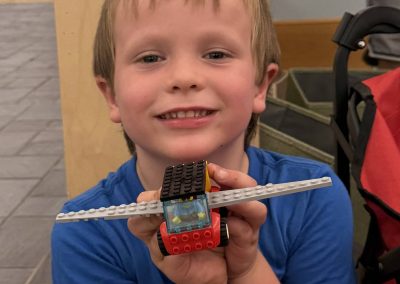 Child holding a LEGO creation that resembles an airplane or vehicle.