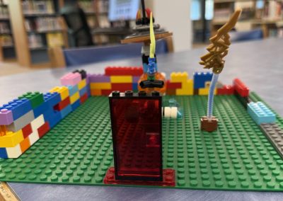 A LEGO structure on a green base plate with colorful walls and an abstract figure, set in the library.