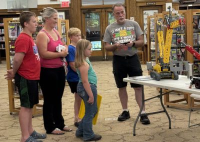 A man demonstrates a LEGO construction to a small group in the library.
