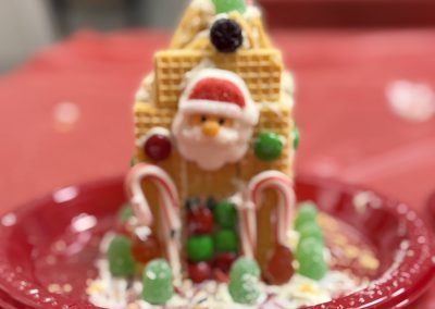 A festive candy house with a Santa face, gumdrops, and candy canes on a red plate.